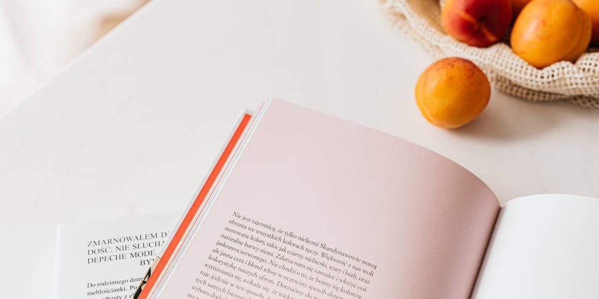 From above of opened book placed on white table near cotton sack with natural ripe apricots