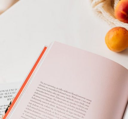 From above of opened book placed on white table near cotton sack with natural ripe apricots