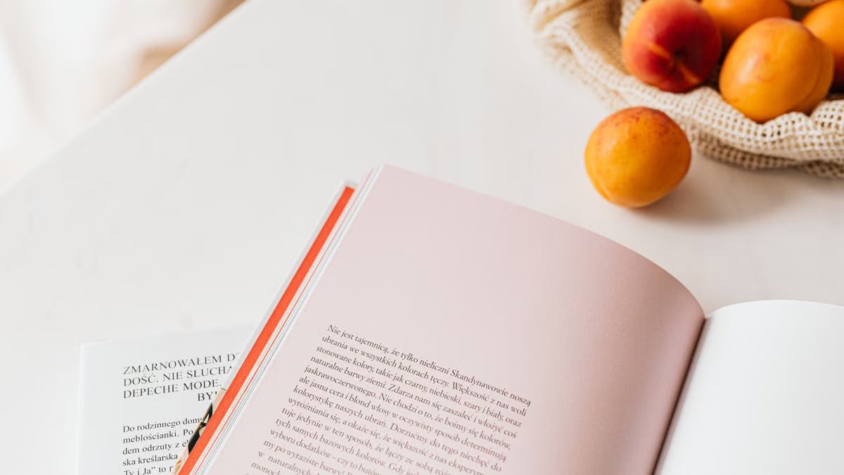 From above of opened book placed on white table near cotton sack with natural ripe apricots