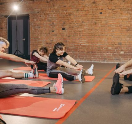 A group of diverse adults stretching on mats in a brick-walled fitness studio.