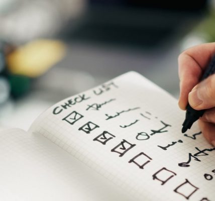 Checklist notebook task progress accuracy. Close-up hand holding pen while marking completed tasks grid notebook. Symbol of productivity, precision, quality control, and workflow management in business or personal planning