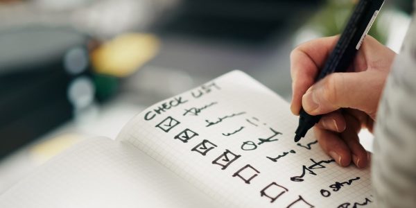 Checklist notebook task progress accuracy. Close-up hand holding pen while marking completed tasks grid notebook. Symbol of productivity, precision, quality control, and workflow management in business or personal planning