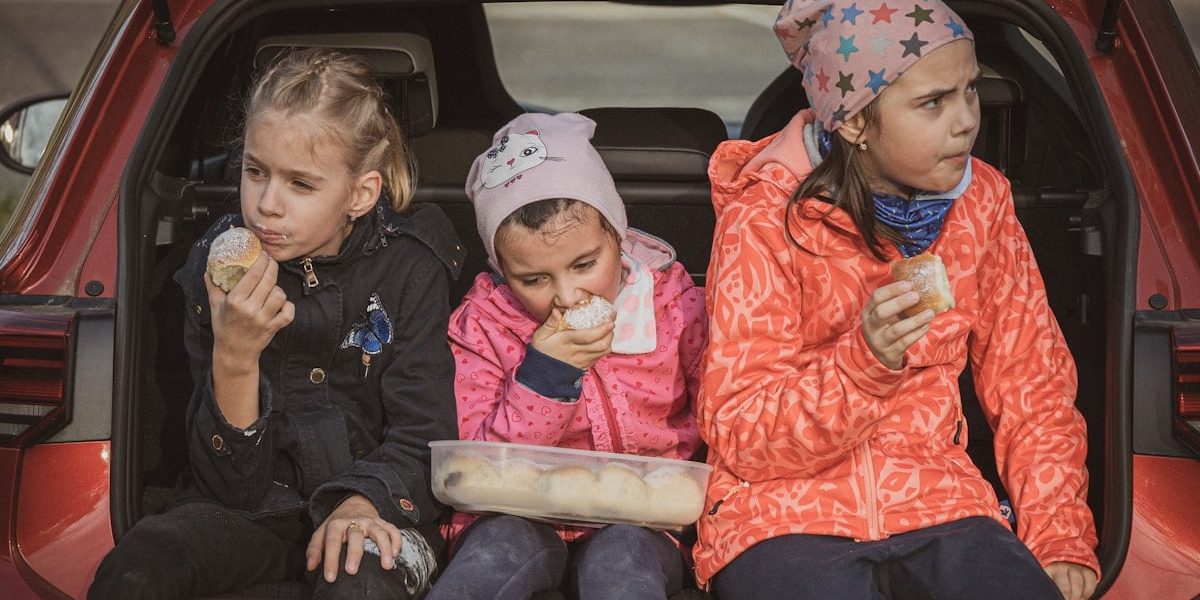 three girls eating buns in the trunk of a car