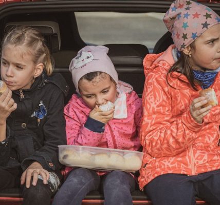 three girls eating buns in the trunk of a car