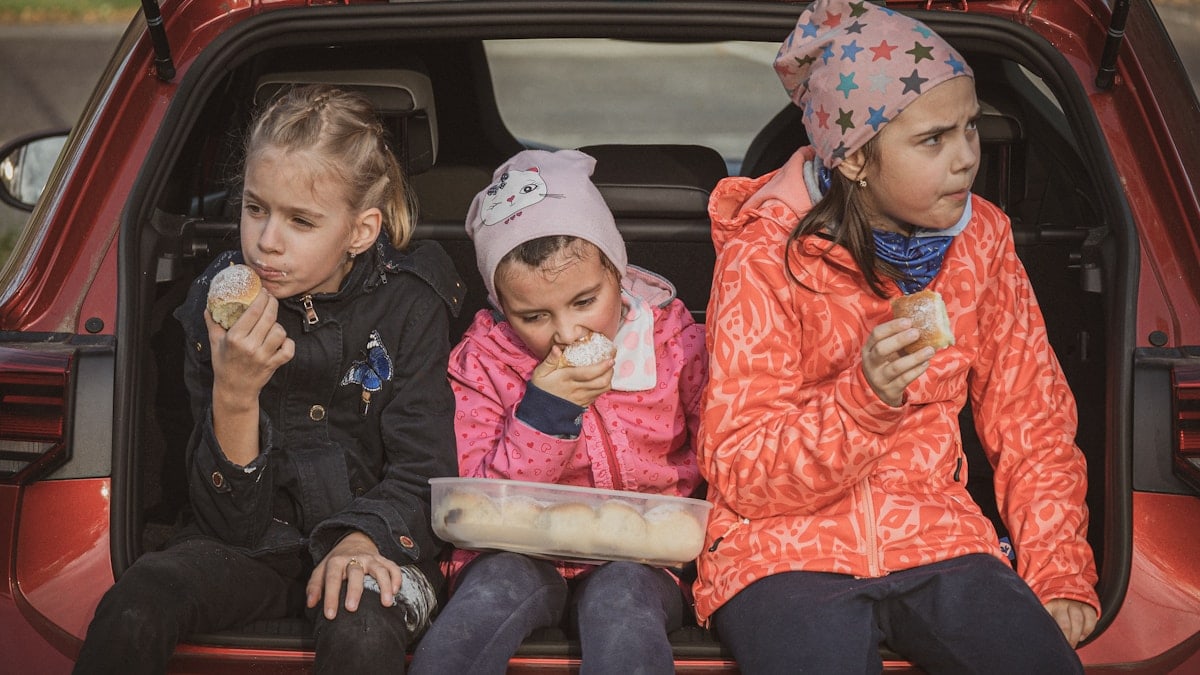 three girls eating buns in the trunk of a car